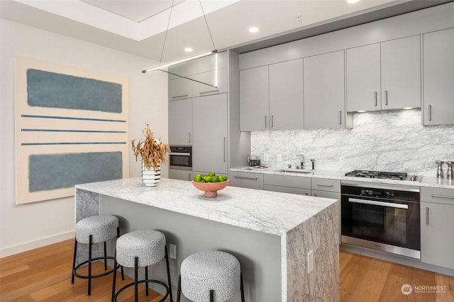 kitchen with appliances with stainless steel finishes, sink, gray cabinetry, a kitchen breakfast bar, and light hardwood / wood-style flooring