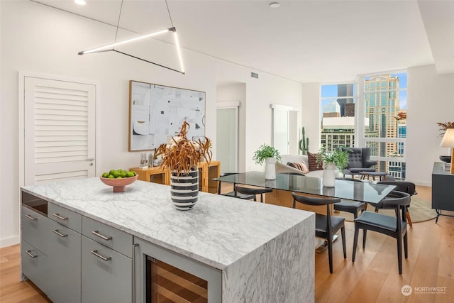 kitchen with gray cabinets, a center island, wine cooler, light stone countertops, and light wood-type flooring