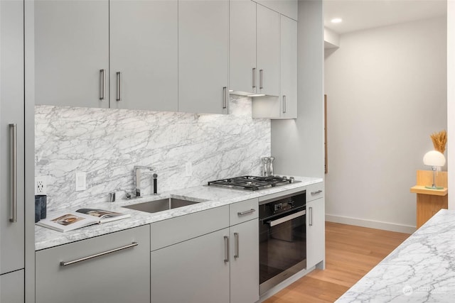 kitchen with sink, oven, decorative backsplash, stainless steel gas cooktop, and light stone counters