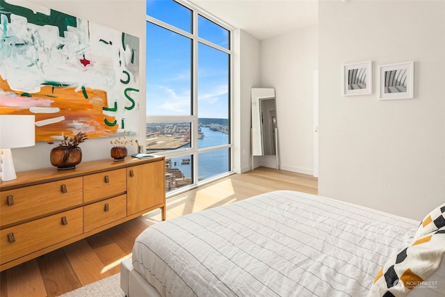 bedroom featuring light hardwood / wood-style flooring, a wall of windows, and a water view