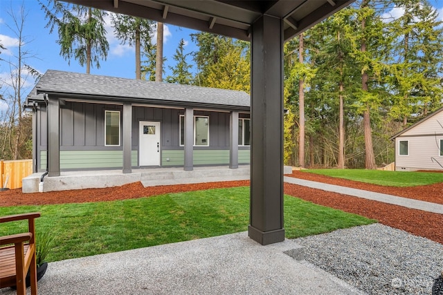 view of front facade with roof with shingles, board and batten siding, covered porch, and a front yard