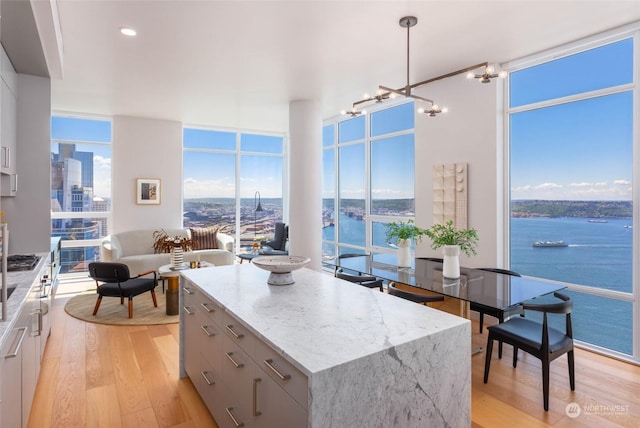 kitchen featuring light hardwood / wood-style flooring, a center island, a water view, light stone counters, and decorative light fixtures