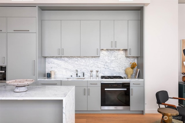 kitchen with gray cabinetry, sink, black oven, and backsplash