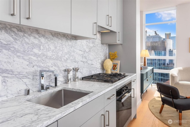 kitchen with appliances with stainless steel finishes, sink, decorative backsplash, light hardwood / wood-style floors, and light stone counters