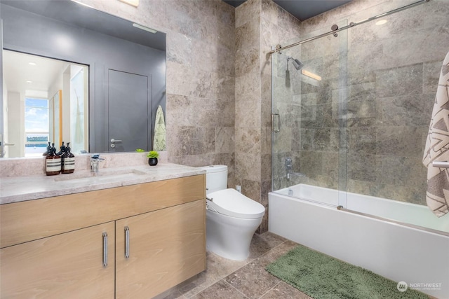 full bathroom featuring vanity, bath / shower combo with glass door, tile walls, and toilet