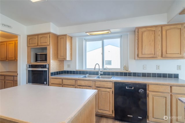 kitchen featuring appliances with stainless steel finishes, sink, a center island, light brown cabinets, and light wood-type flooring