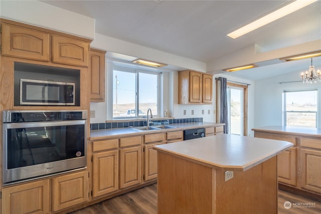 kitchen with sink, vaulted ceiling, appliances with stainless steel finishes, a kitchen island, and light hardwood / wood-style floors