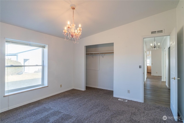 unfurnished bedroom featuring dark colored carpet, lofted ceiling, an inviting chandelier, and a closet