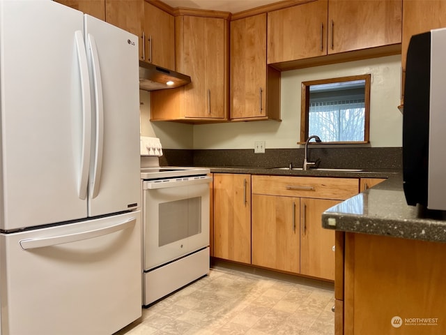 kitchen featuring white appliances, dark stone counters, and sink