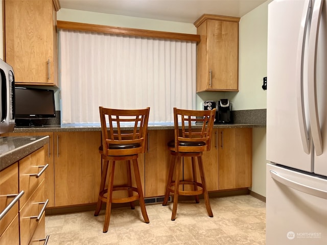 kitchen featuring dark stone counters, a kitchen breakfast bar, and white fridge