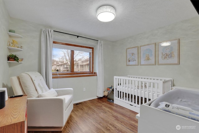 bedroom with light hardwood / wood-style flooring, a nursery area, and a textured ceiling