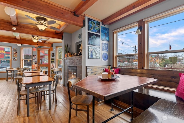 dining area with beamed ceiling, ceiling fan, a fireplace, and light hardwood / wood-style flooring