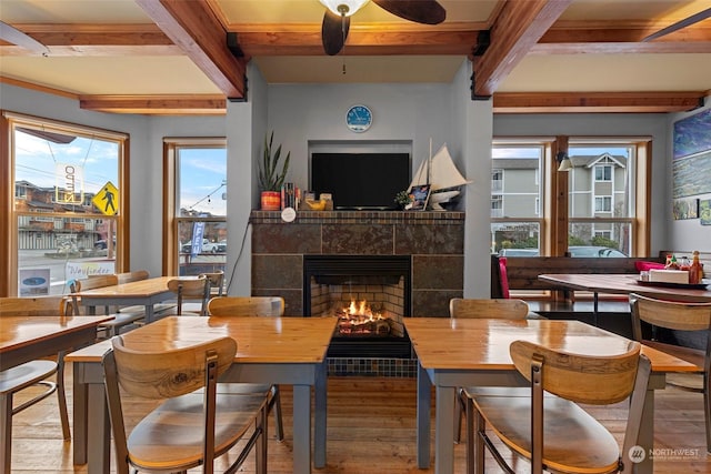 dining space with ceiling fan, light hardwood / wood-style flooring, a tile fireplace, and beamed ceiling