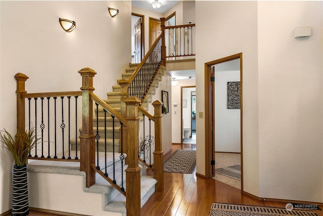 stairway with wood-type flooring and a high ceiling