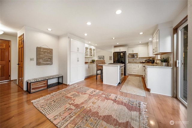 kitchen with a kitchen bar, a center island, light wood-type flooring, stainless steel microwave, and white cabinets