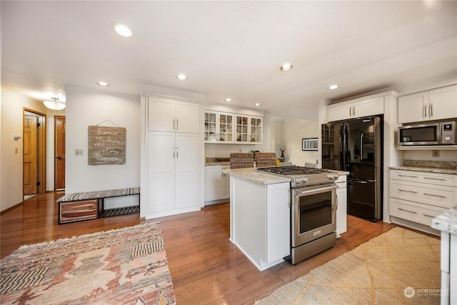 kitchen with a kitchen island, appliances with stainless steel finishes, white cabinets, light stone counters, and light hardwood / wood-style flooring