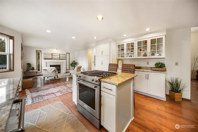 kitchen featuring stainless steel range, light hardwood / wood-style flooring, light stone countertops, and white cabinets