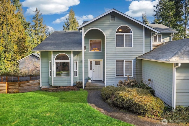 traditional-style home featuring a shingled roof, a front yard, and fence