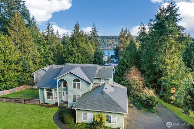 view of front facade featuring aphalt driveway, a shingled roof, a front yard, fence, and a forest view