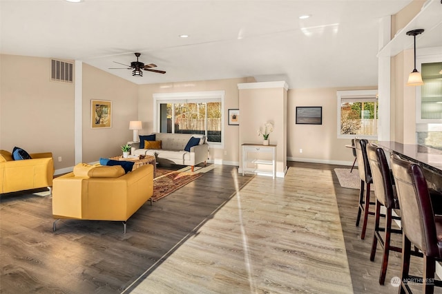 living area with vaulted ceiling, wood finished floors, visible vents, and baseboards