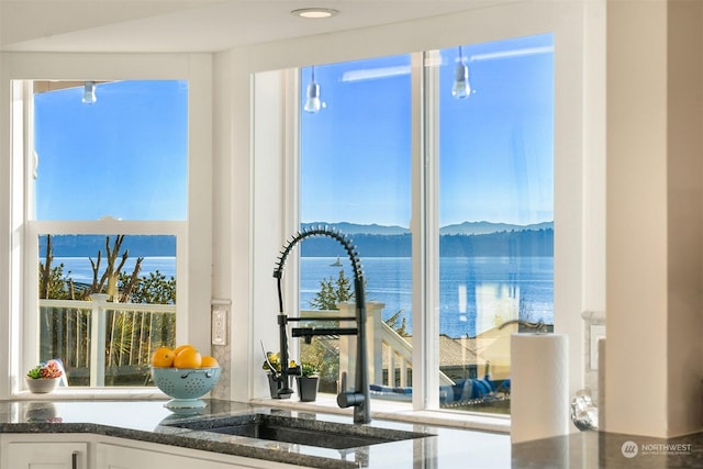 kitchen featuring dark stone counters, a sink, a water and mountain view, and white cabinets