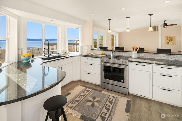 kitchen with a peninsula, a sink, white cabinetry, stainless steel electric range, and dark stone countertops