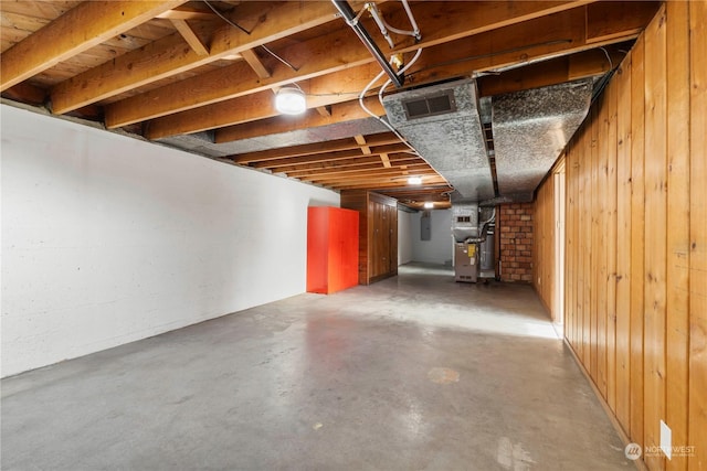 basement featuring heating unit, wooden walls, and electric panel