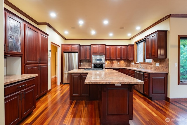 kitchen with sink, stainless steel appliances, light stone countertops, a kitchen island, and dark hardwood / wood-style flooring