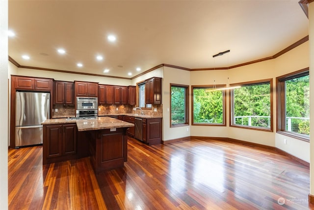 kitchen with dark hardwood / wood-style flooring, decorative backsplash, a center island, stainless steel appliances, and light stone countertops