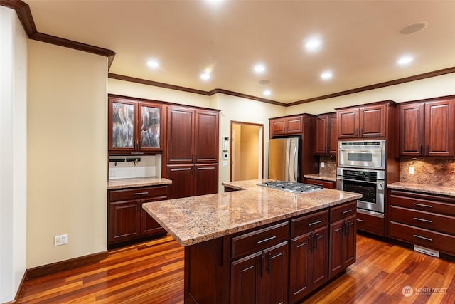 kitchen featuring decorative backsplash, a center island, stainless steel appliances, light stone countertops, and dark wood-type flooring