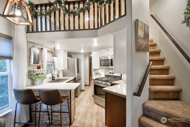 kitchen with white cabinetry, appliances with stainless steel finishes, light hardwood / wood-style floors, and a high ceiling