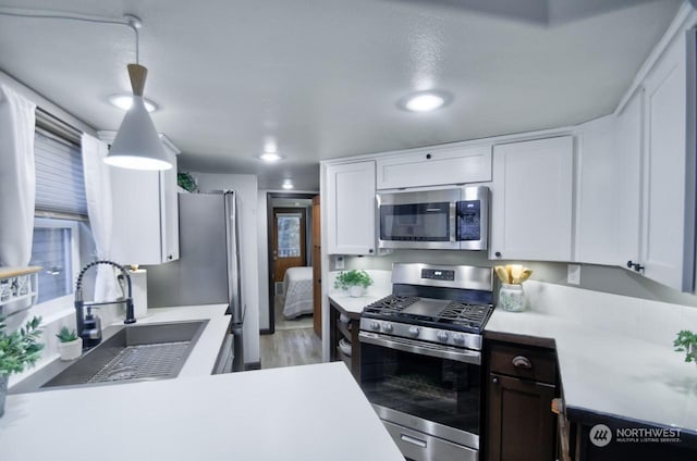 kitchen featuring pendant lighting, sink, light hardwood / wood-style flooring, appliances with stainless steel finishes, and white cabinets