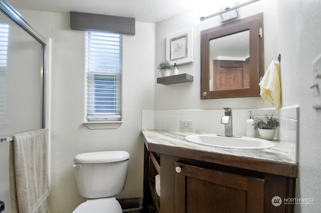 bathroom featuring tasteful backsplash, vanity, toilet, and a shower with shower door