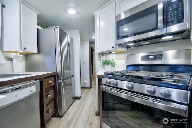 kitchen with stainless steel appliances, light hardwood / wood-style floors, and white cabinets