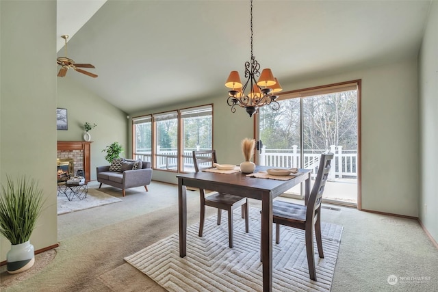 dining room featuring ceiling fan with notable chandelier, light colored carpet, a fireplace, and high vaulted ceiling