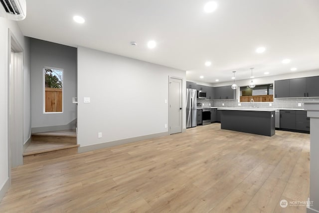 kitchen featuring appliances with stainless steel finishes, a center island, tasteful backsplash, decorative light fixtures, and light wood-type flooring