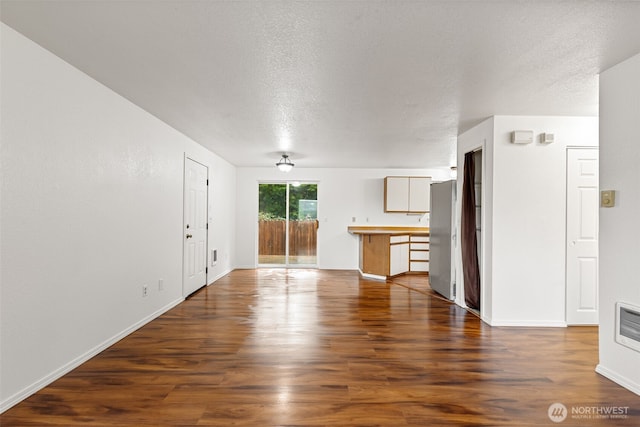 unfurnished living room with a textured ceiling, dark wood-type flooring, and baseboards