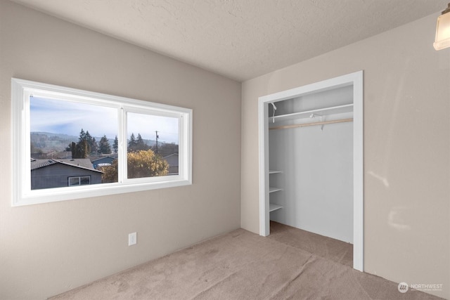 unfurnished bedroom with light colored carpet, a closet, and a textured ceiling