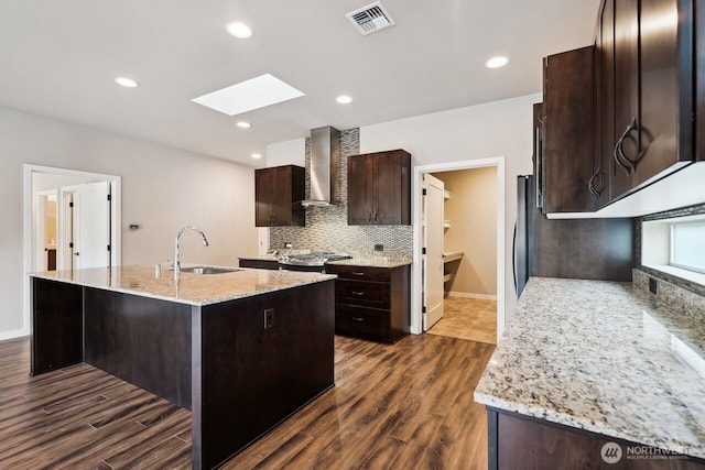 kitchen featuring dark brown cabinetry, a skylight, a sink, visible vents, and wall chimney range hood