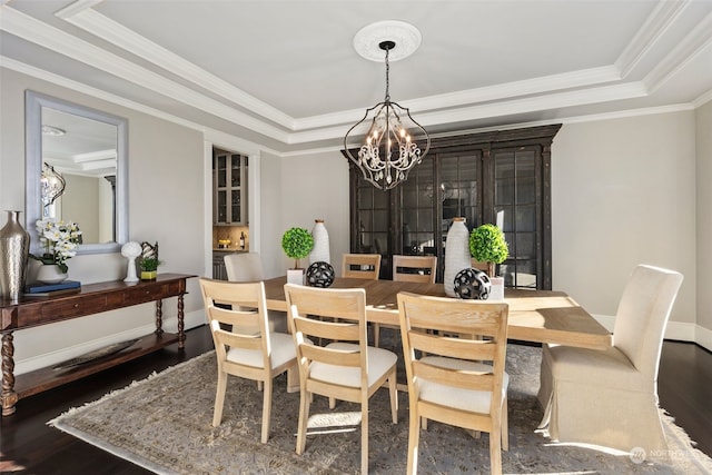 dining area featuring dark wood-type flooring, ornamental molding, a raised ceiling, and a notable chandelier