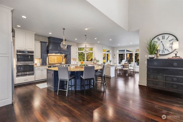 kitchen featuring a kitchen island, double oven, white cabinetry, a kitchen bar, and light stone countertops