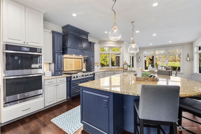 kitchen with pendant lighting, white cabinets, light stone counters, stainless steel appliances, and blue cabinetry