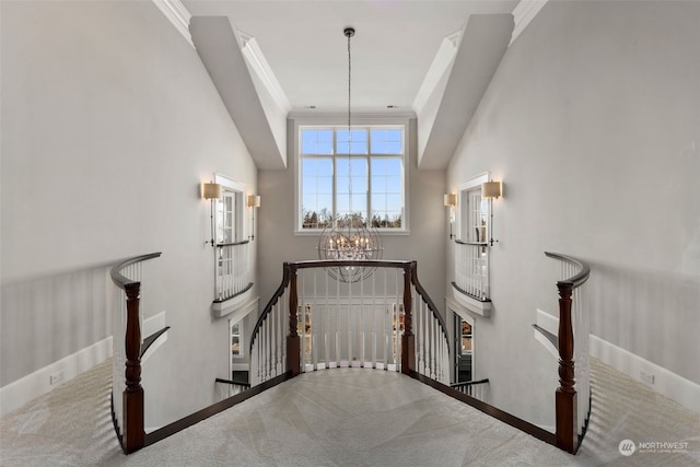 staircase featuring an inviting chandelier, a towering ceiling, ornamental molding, and carpet floors