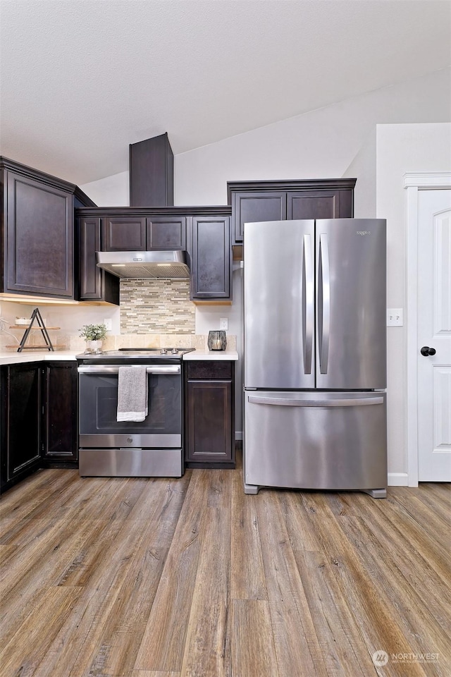 kitchen with dark brown cabinetry, vaulted ceiling, light hardwood / wood-style flooring, stainless steel appliances, and backsplash