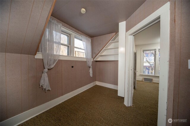 bonus room with dark colored carpet, visible vents, and wood walls