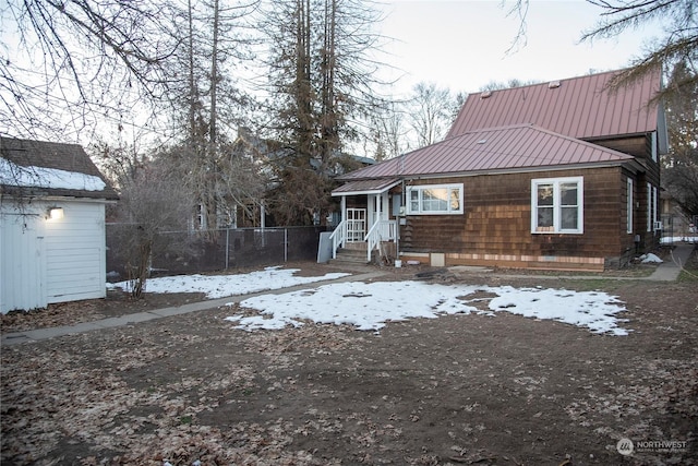 snow covered rear of property featuring metal roof and fence