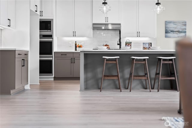 6612 6th St E, Tacoma, WA 98424 - kitchen with light wood-type flooring, gray cabinets, stainless steel double oven, backsplash, and a kitchen breakfast bar
