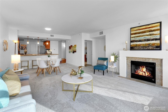 carpeted living area featuring a high end fireplace, visible vents, and baseboards