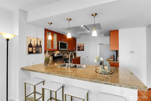 kitchen featuring tile counters, appliances with stainless steel finishes, glass insert cabinets, a sink, and a peninsula