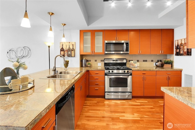 kitchen featuring light wood-style flooring, appliances with stainless steel finishes, a peninsula, a sink, and backsplash